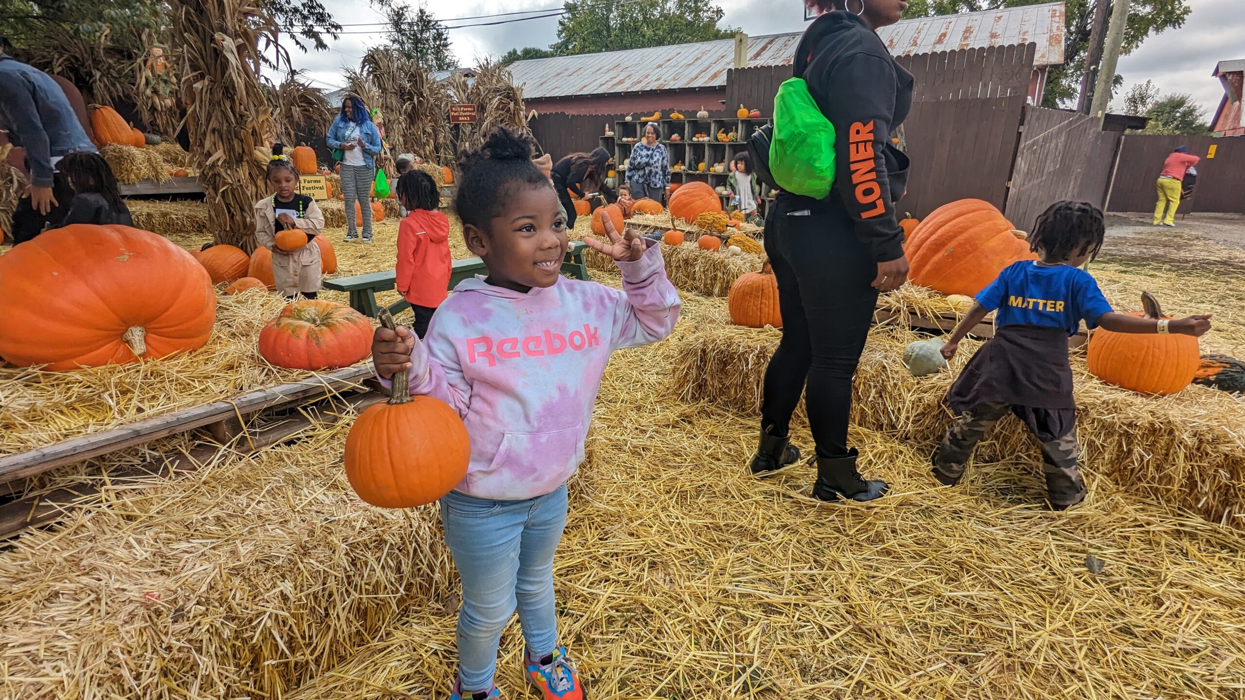 Girl holds up pumpkin and peace sign at cox farms.