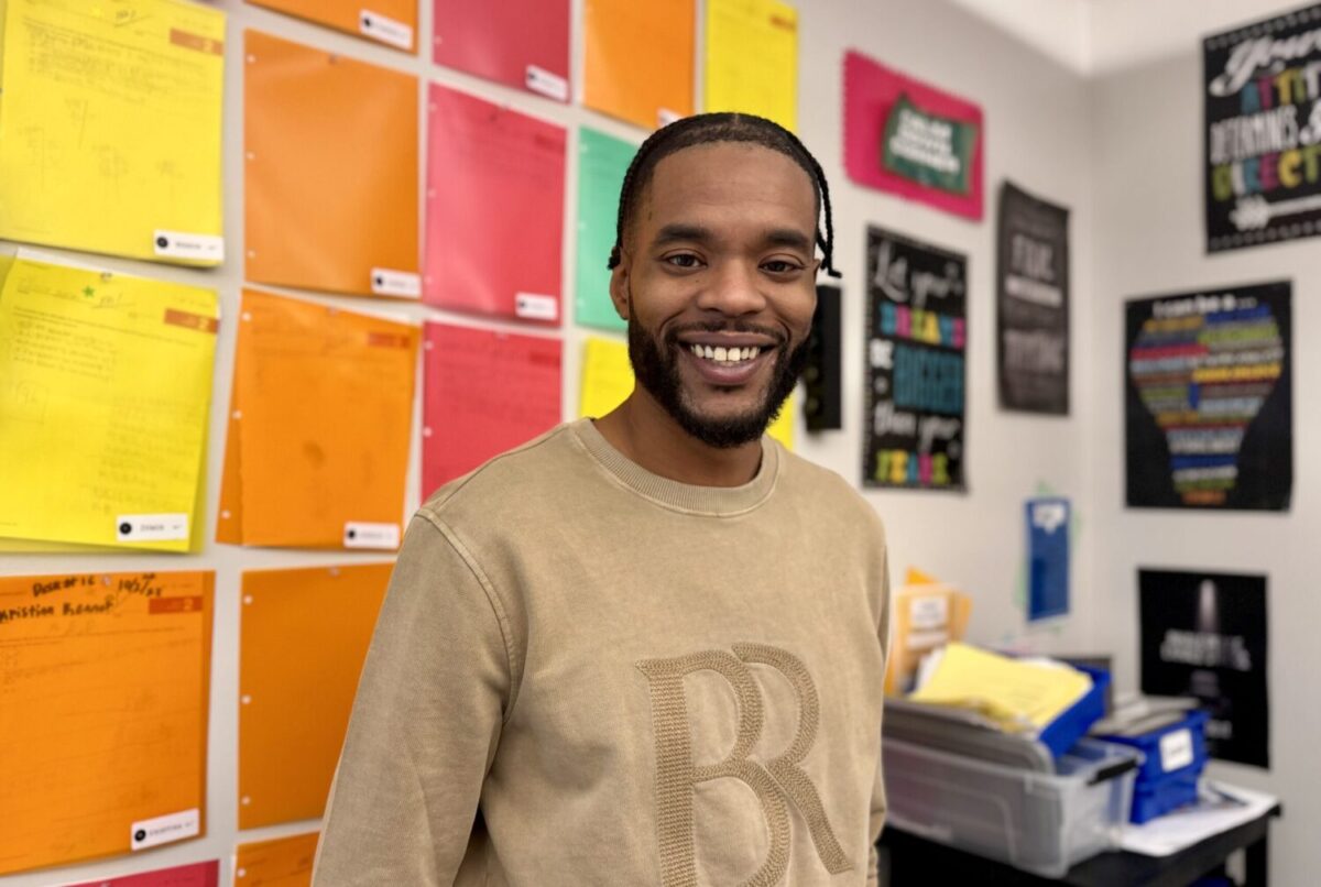 Mr. Miles Edwards smiling into the camera inside his classroom